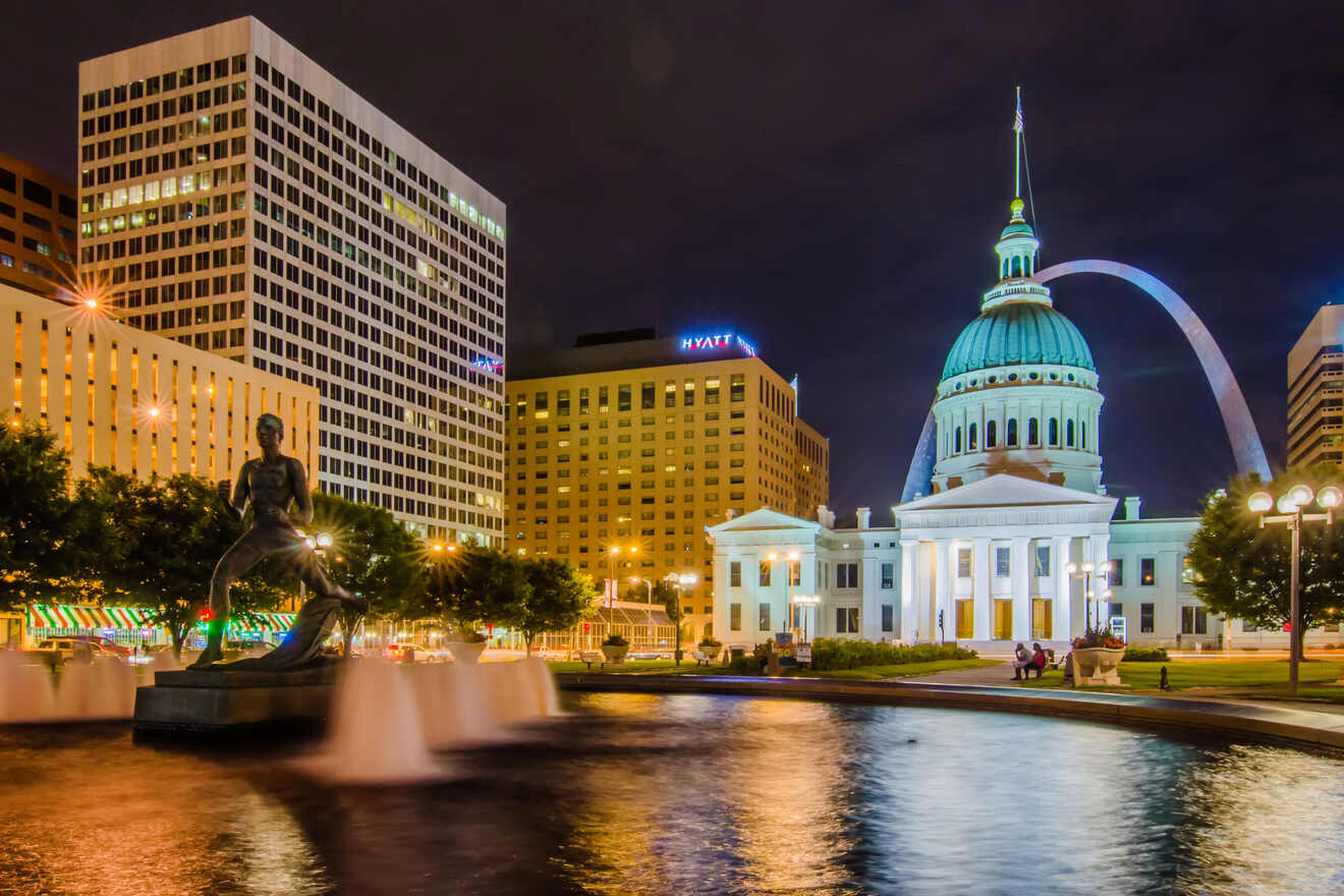 A night view of a cityscape with a lit-up capitol building dome, a fountain statue in the foreground, and an arch monument in the distance